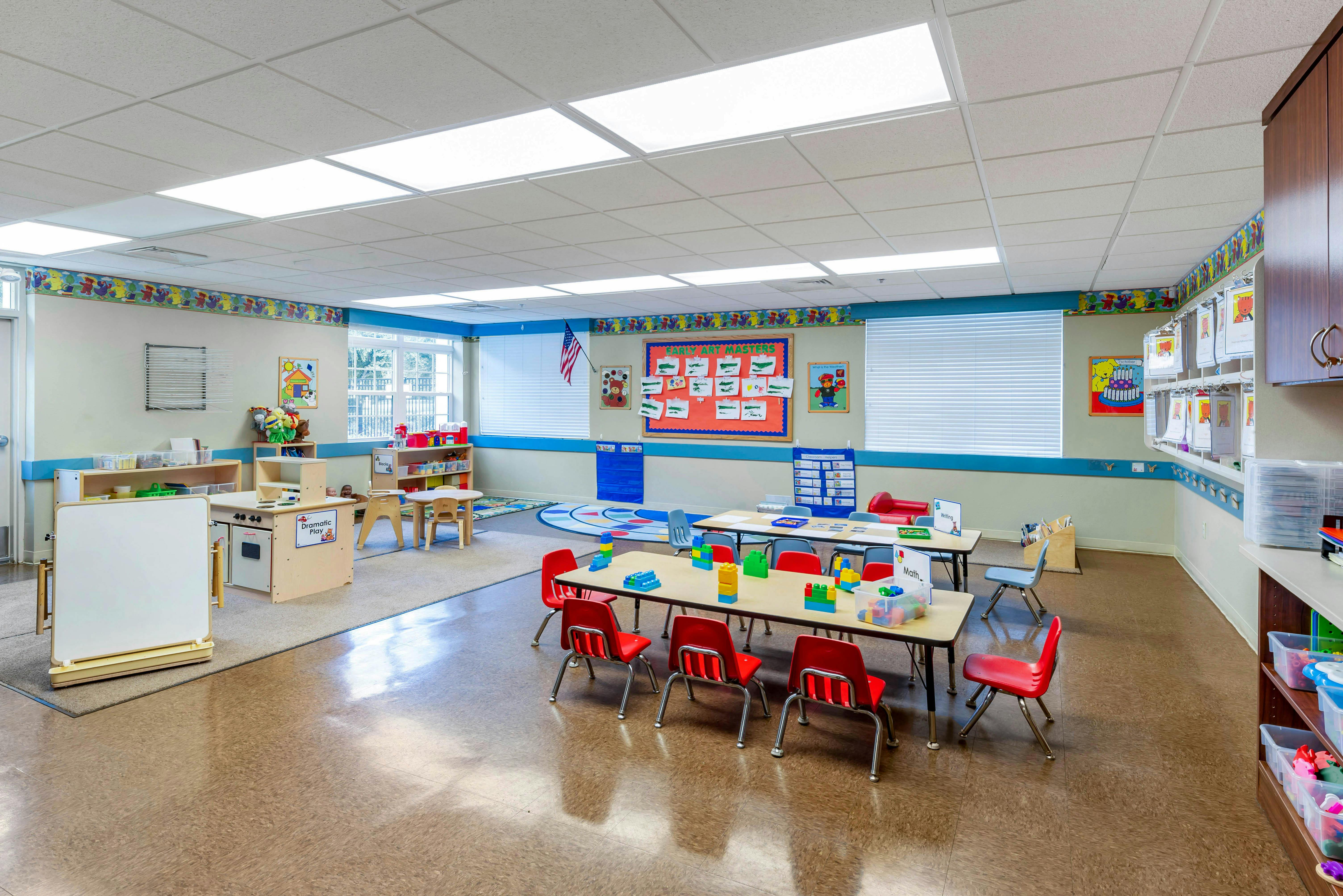 Colorful classroom with child-sized tables, chairs, play kitchen, and educational posters