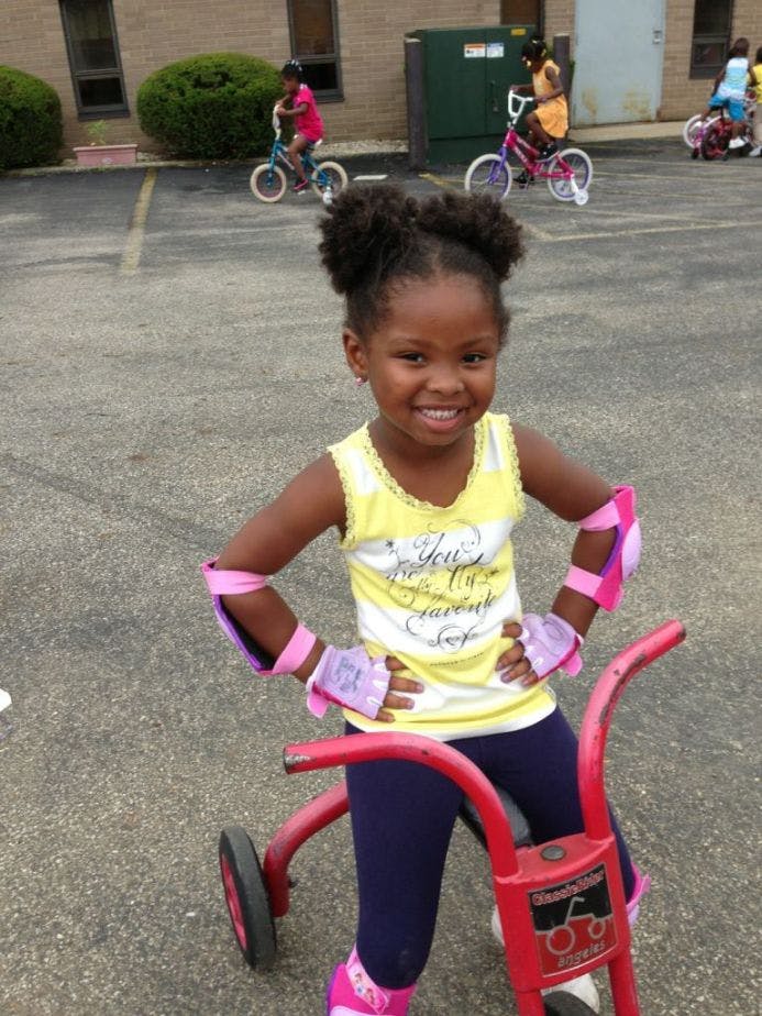 Child wearing elbow and knee pads standing with a tricycle