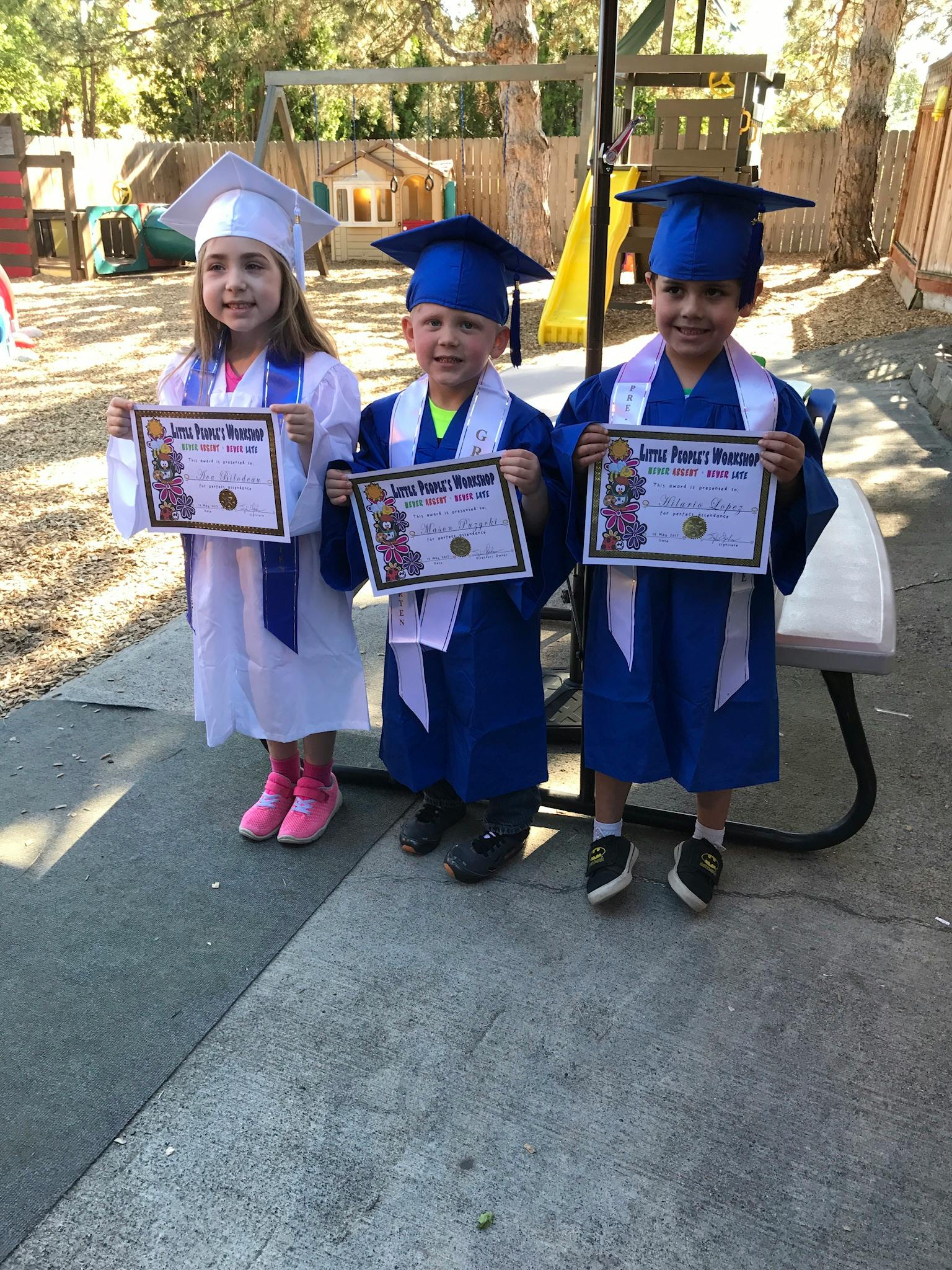 Three children in graduation caps and gowns holding certificates