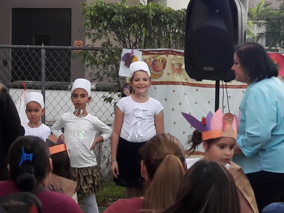 Three children in white hats standing with an adult nearby