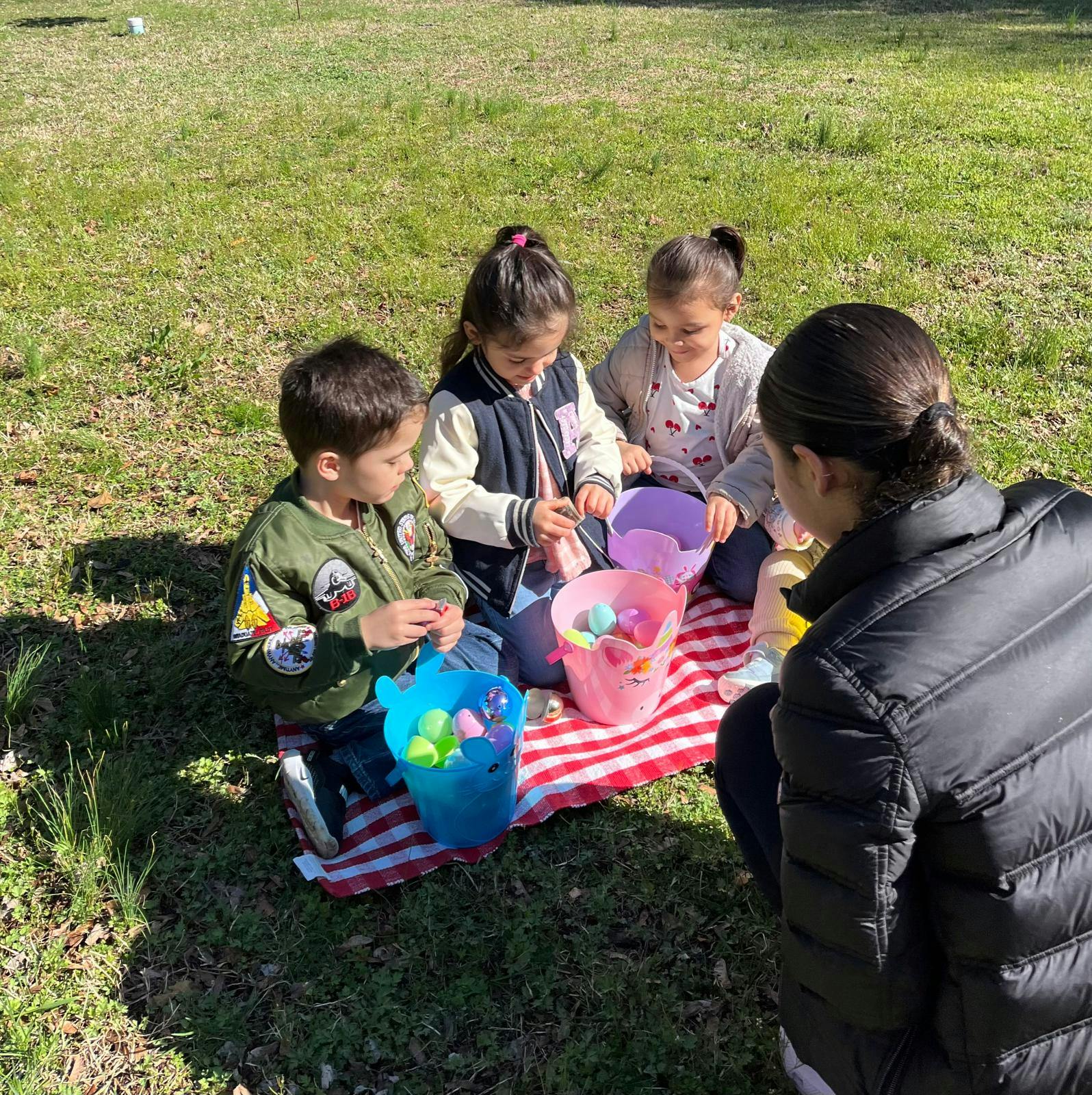 People sitting on a picnic blanket with buckets of colorful plastic eggs