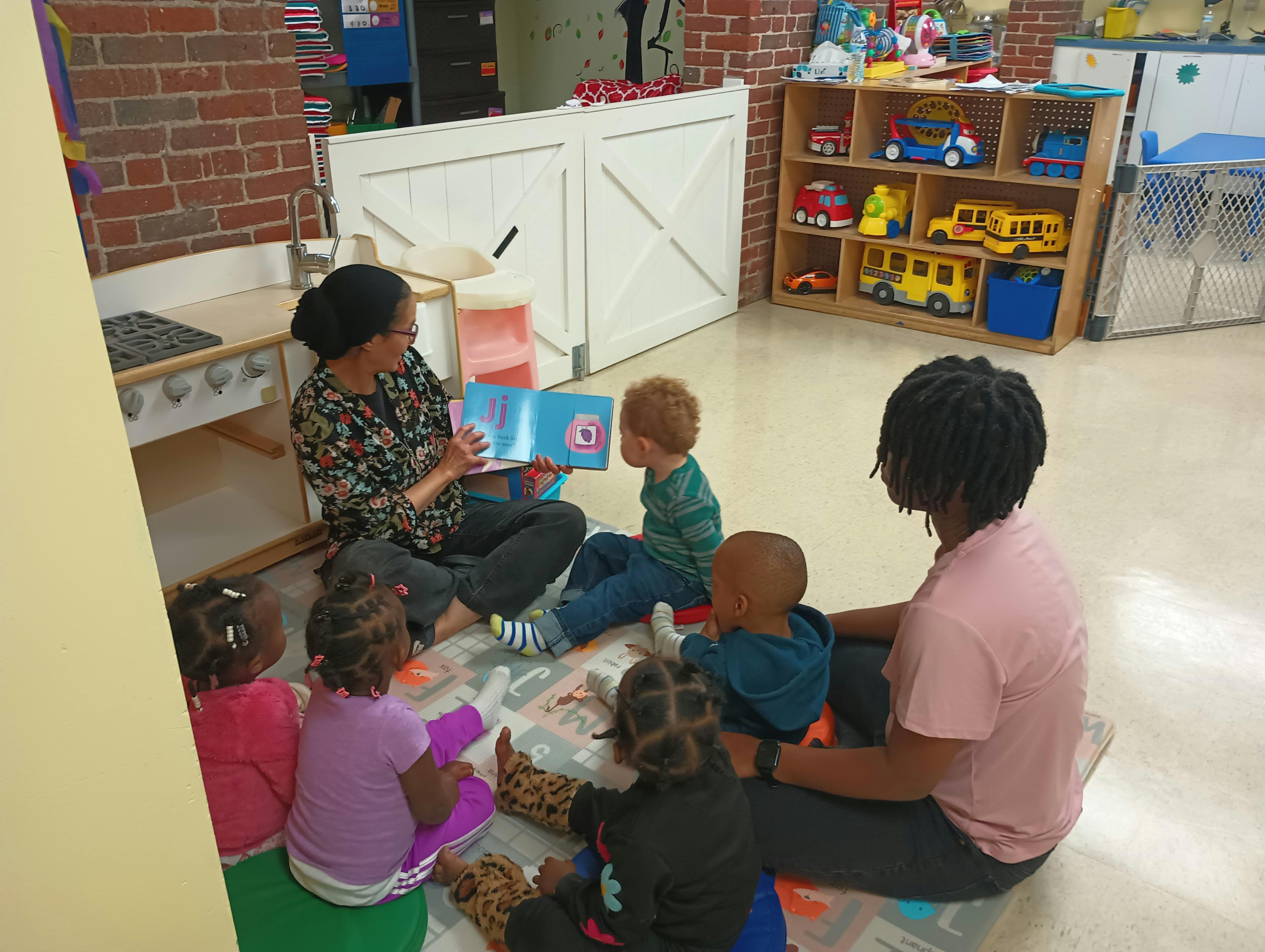 Adult reading a book to a group of children in a classroom