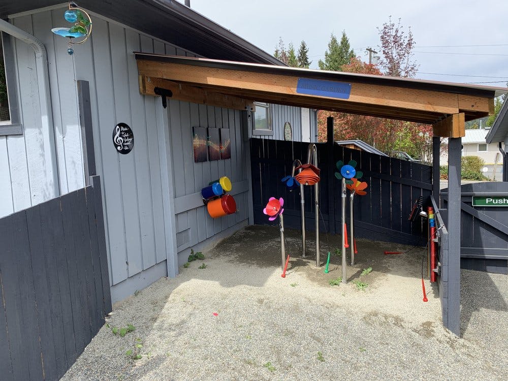 Outdoor play area with sand, colorful buckets, and a wooden shelter