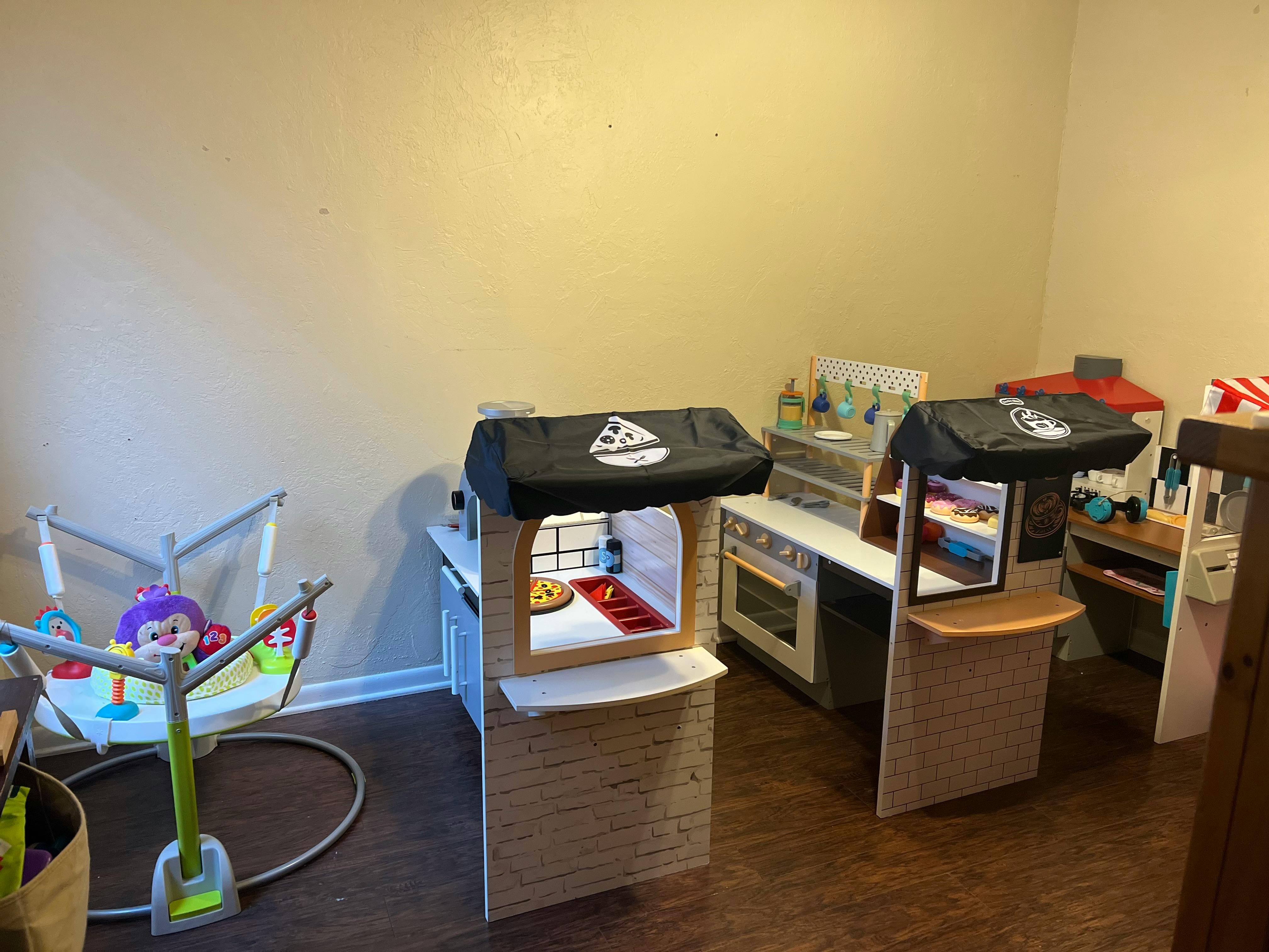 Play kitchen and pizza stand in a room with a baby bouncer