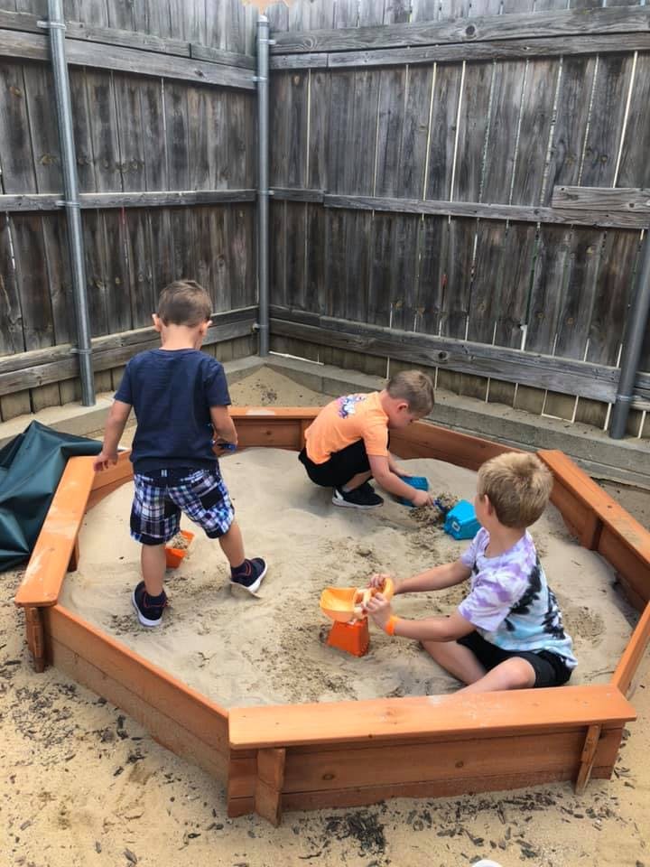 Three children playing in a sandbox with toys