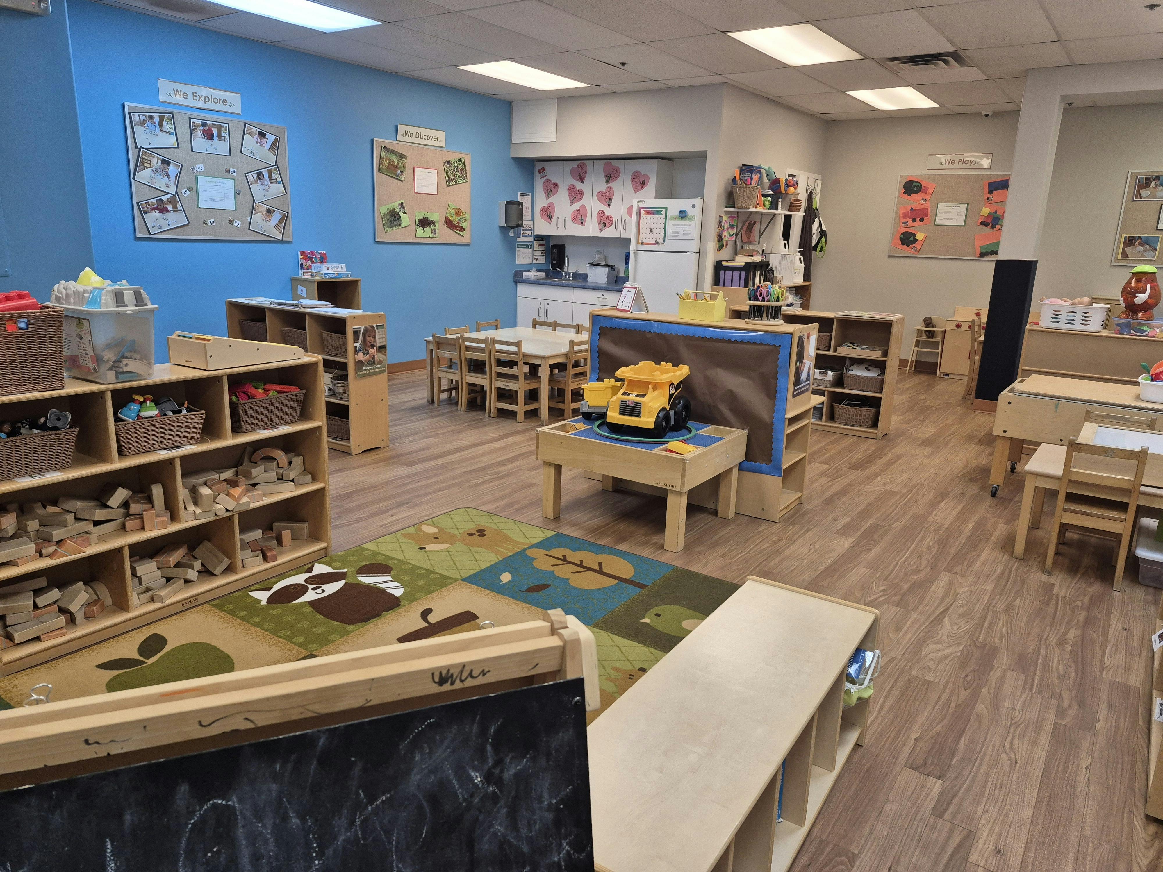 A classroom with wooden shelves filled with blocks, tables, and a rug with animal designs