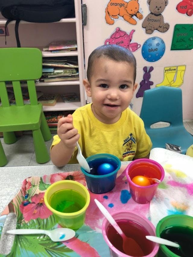 Child holding a spoon over a cup with a blue egg in liquid