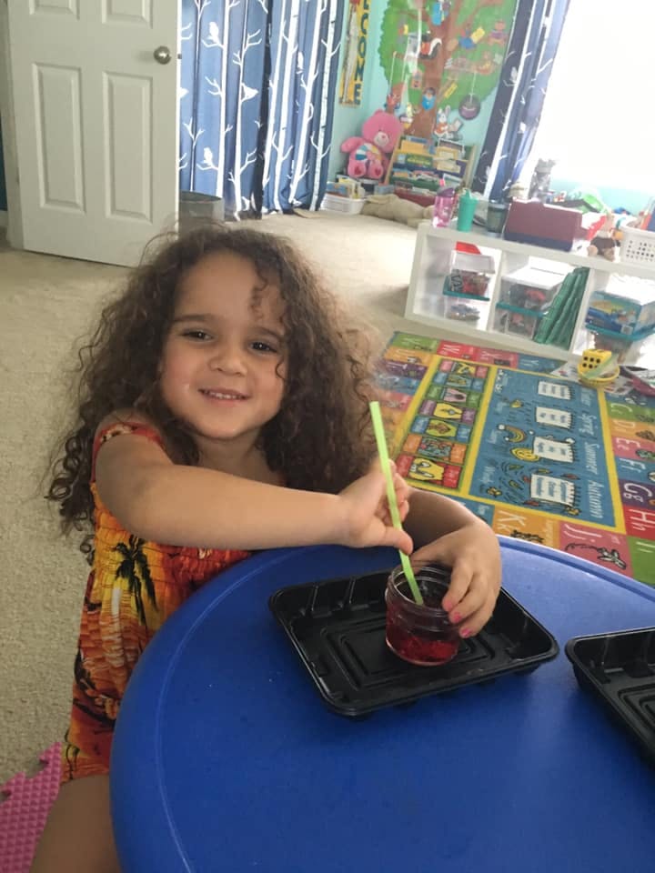 Child with curly hair holding a straw in a drink at a blue table