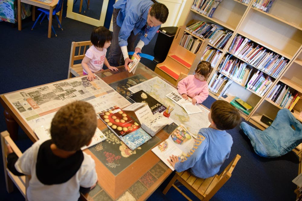 Adult and three children at a table with books and games in a room with bookshelves