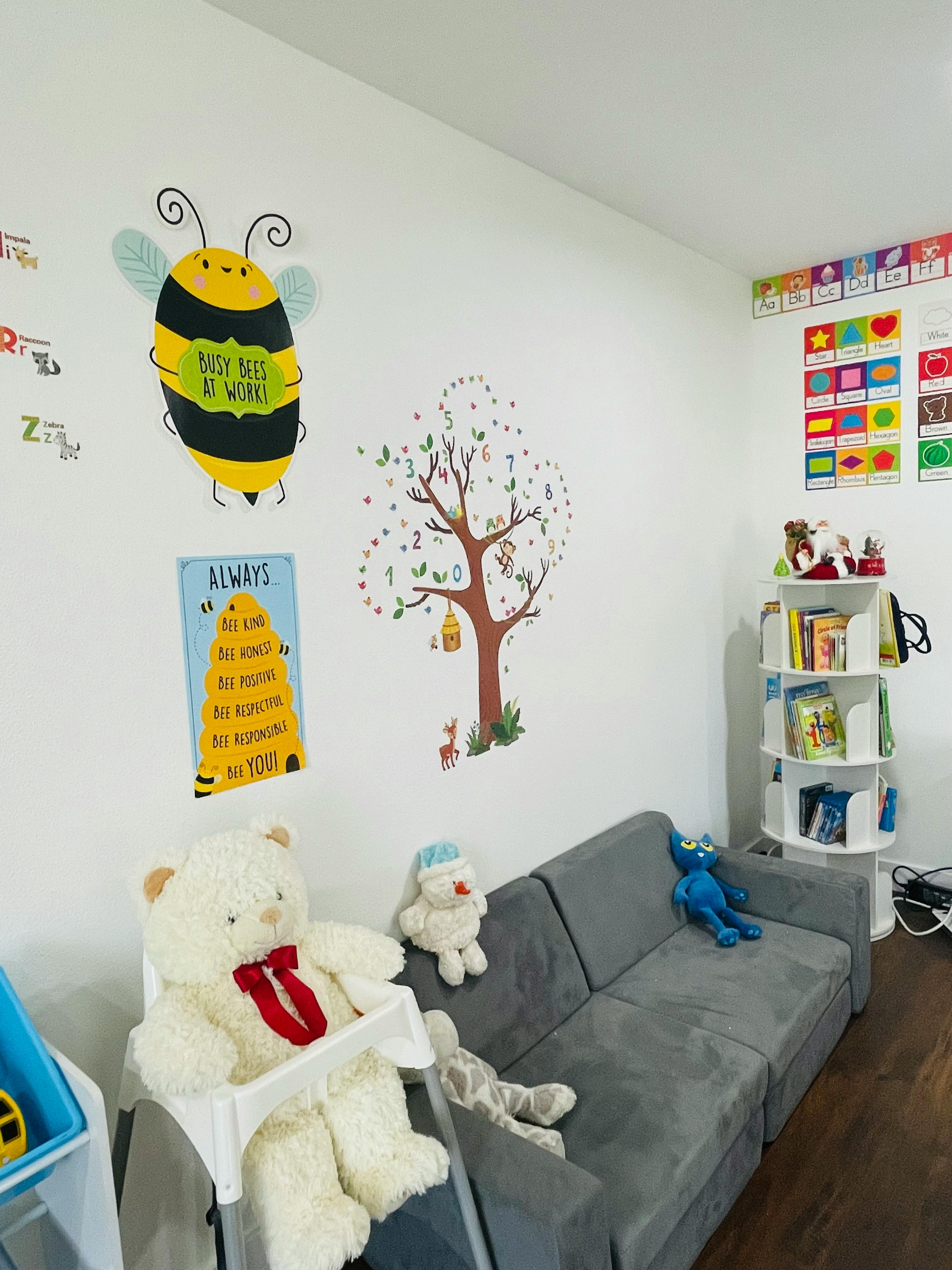 Wall with bee and tree decals, gray couch, and white bookshelf