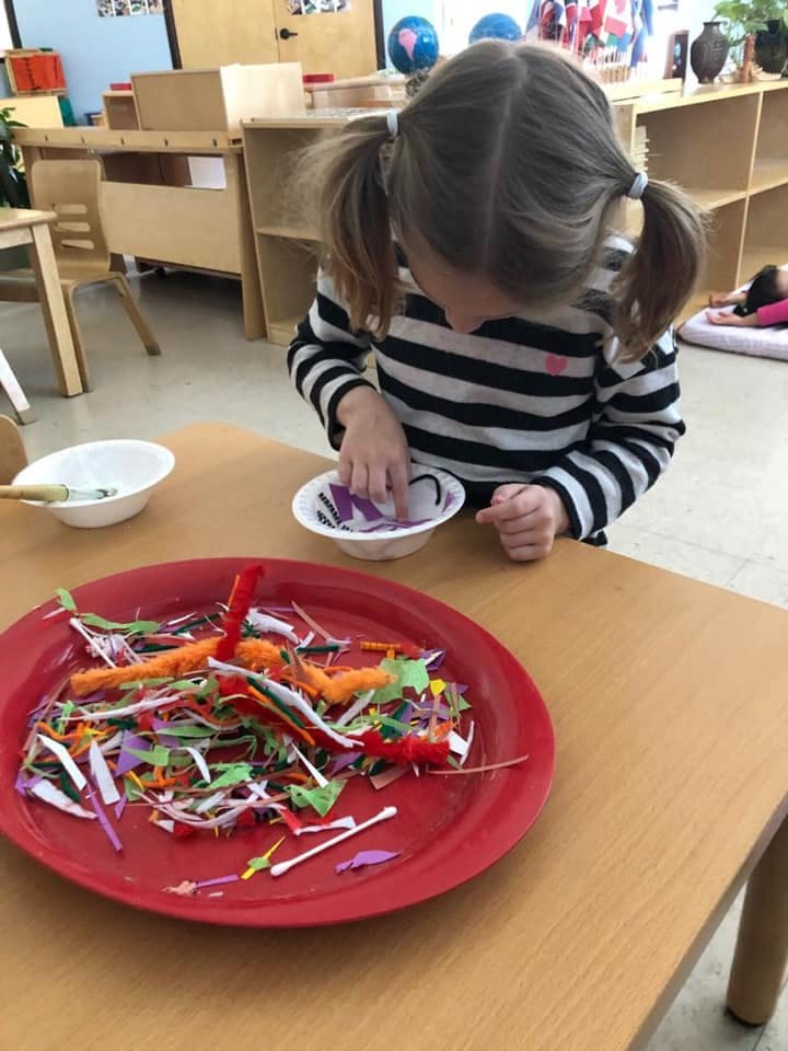 Child with pigtails sorting small craft pieces into a bowl