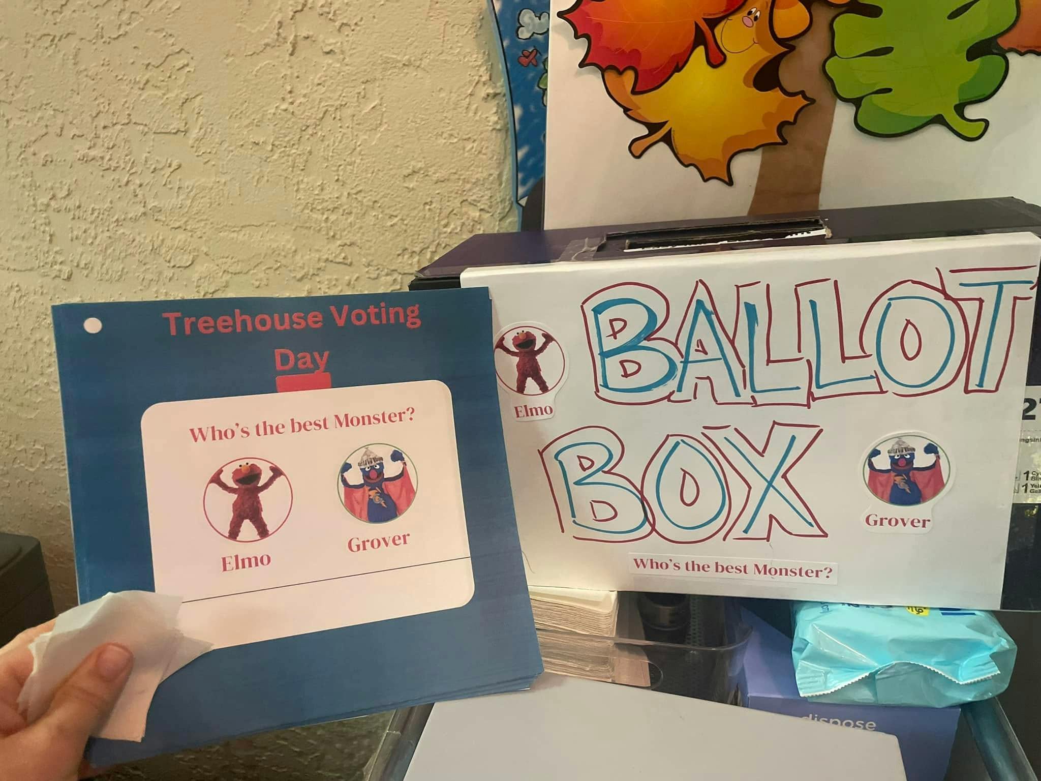 Child's hand holding a voting ballot next to a ballot box