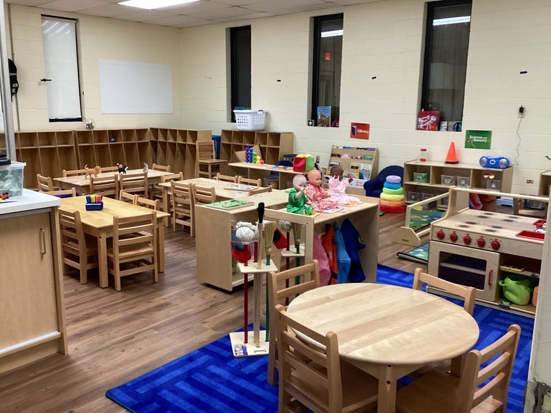 Classroom with small wooden tables and chairs, cubbies, play kitchen, and toys