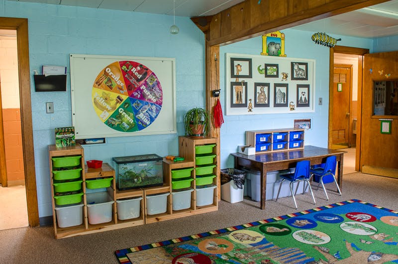 Classroom with colorful rug, tables, chairs, and storage units