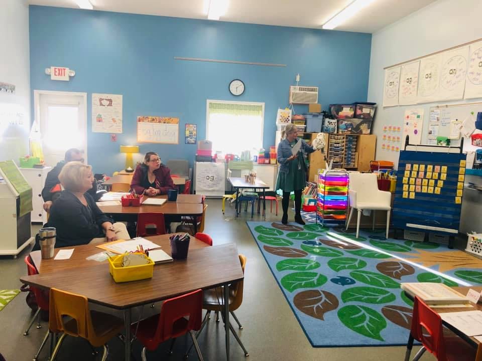 People in a classroom with tables and a rug