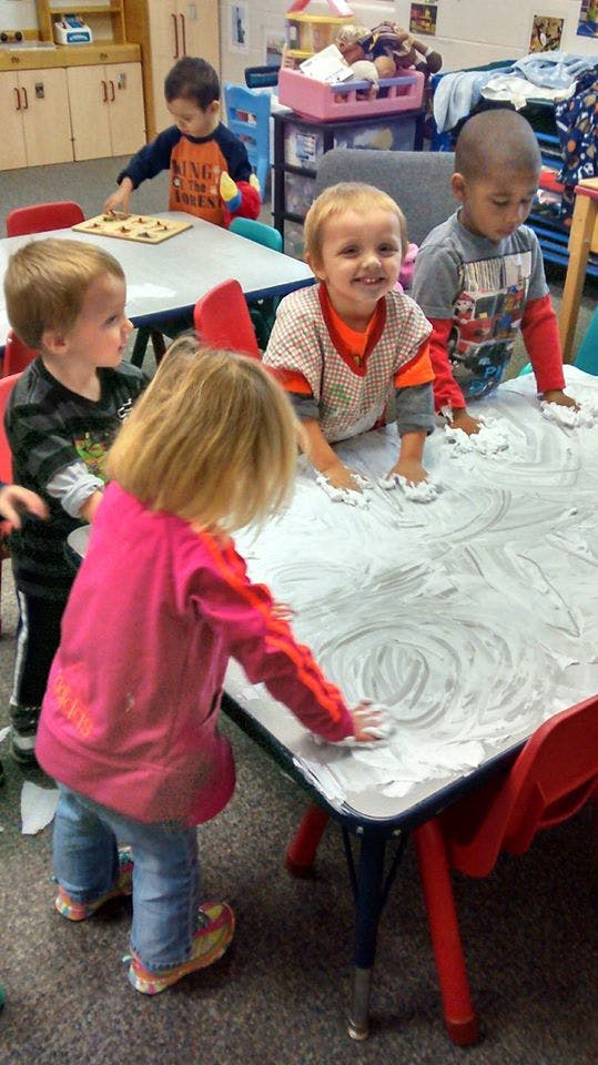 Children playing with shaving cream on a table in a classroom