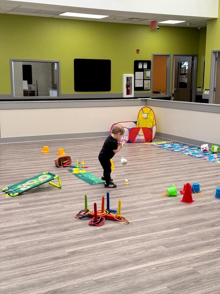 Child playing with a toy golf club in a room with other toys