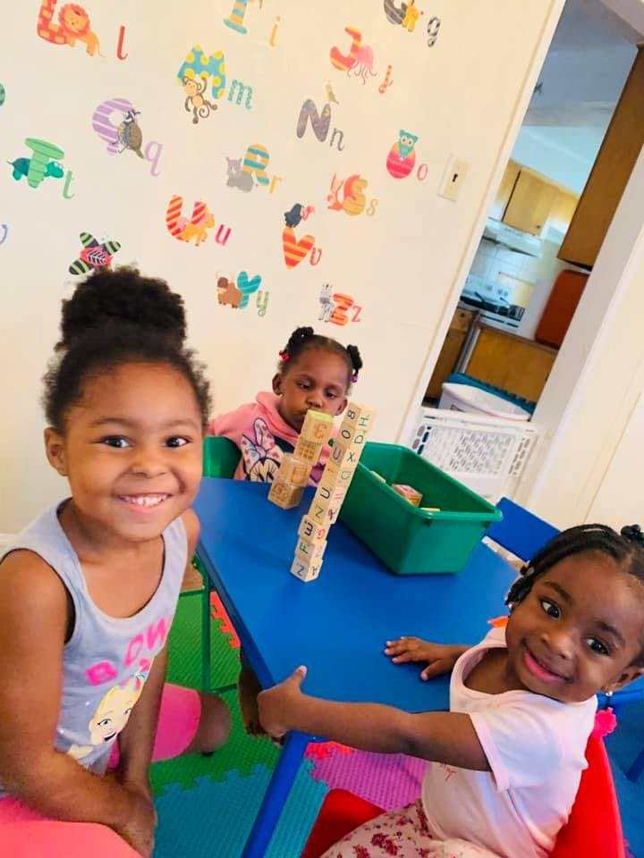 Three children at a table, one playing with blocks, two looking at camera