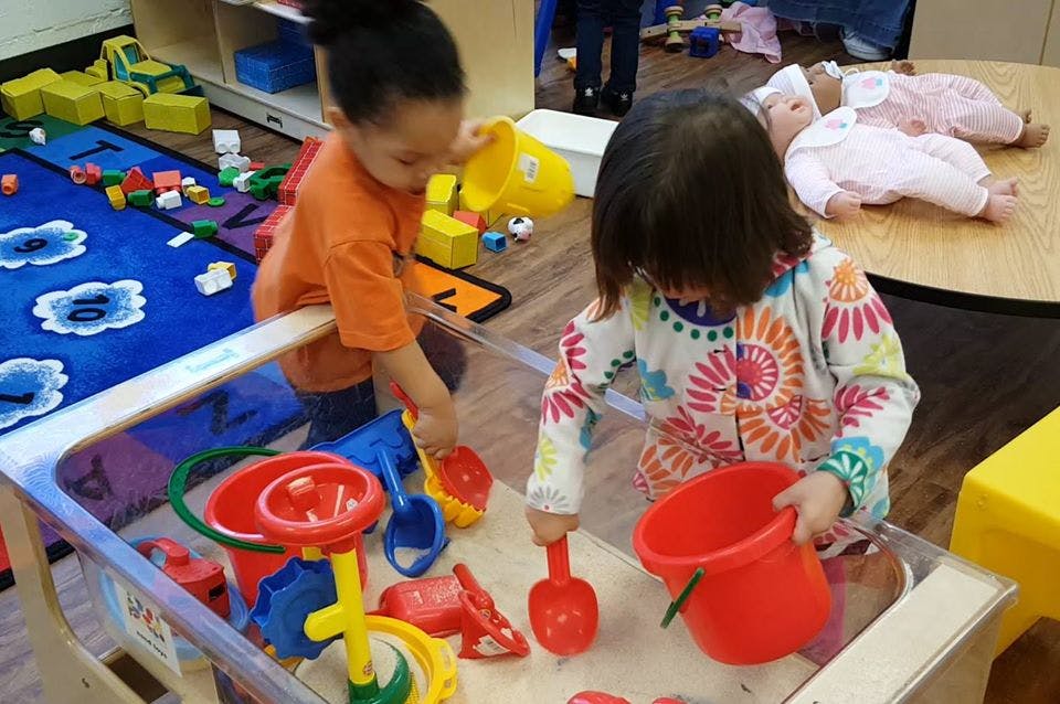 Two children playing with sand toys in a sensory table