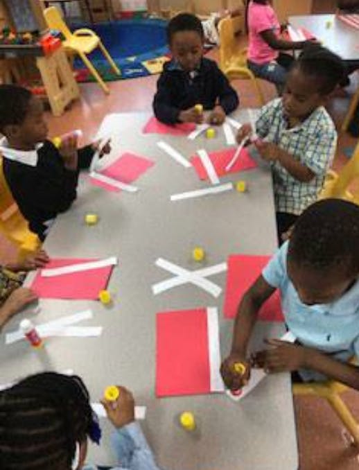 Children at a table doing a craft with red paper and white strips