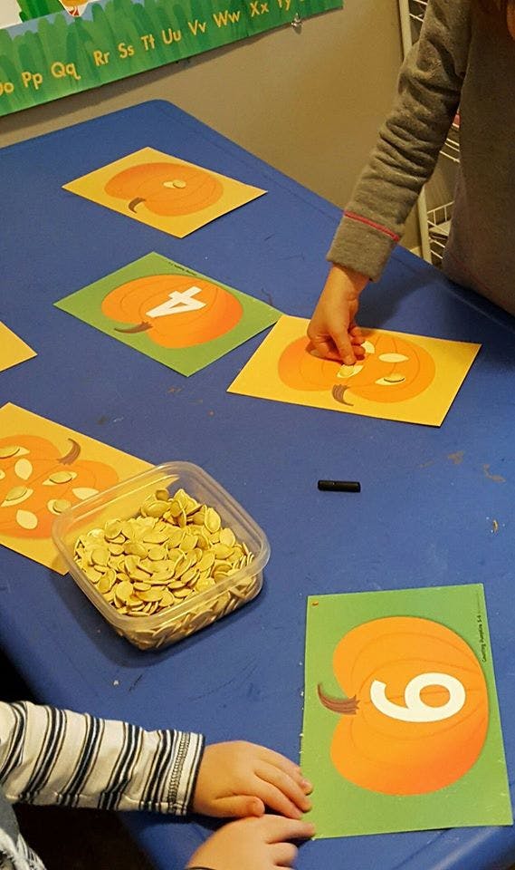 Child placing pumpkin seeds on a pumpkin-themed number card