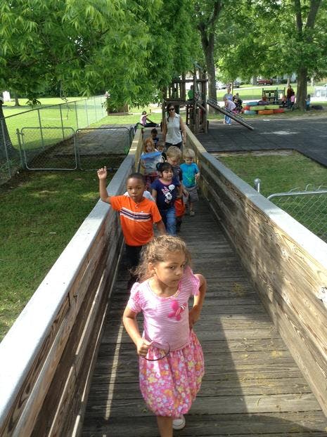 Children and an adult walking on a wooden walkway outdoors
