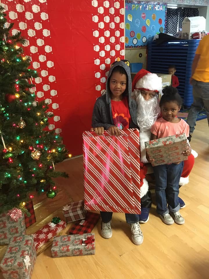 Two children and a person dressed as Santa holding wrapped gifts next to a Christmas tree