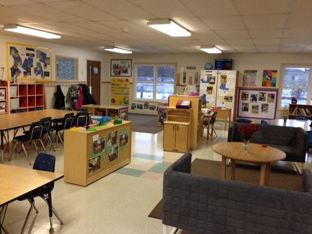 Classroom with tables, chairs, and shelves, featuring a cozy seating area