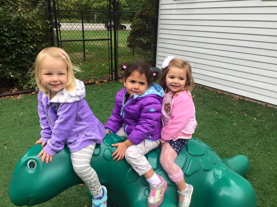 Three children sitting on a green dinosaur-shaped playground toy