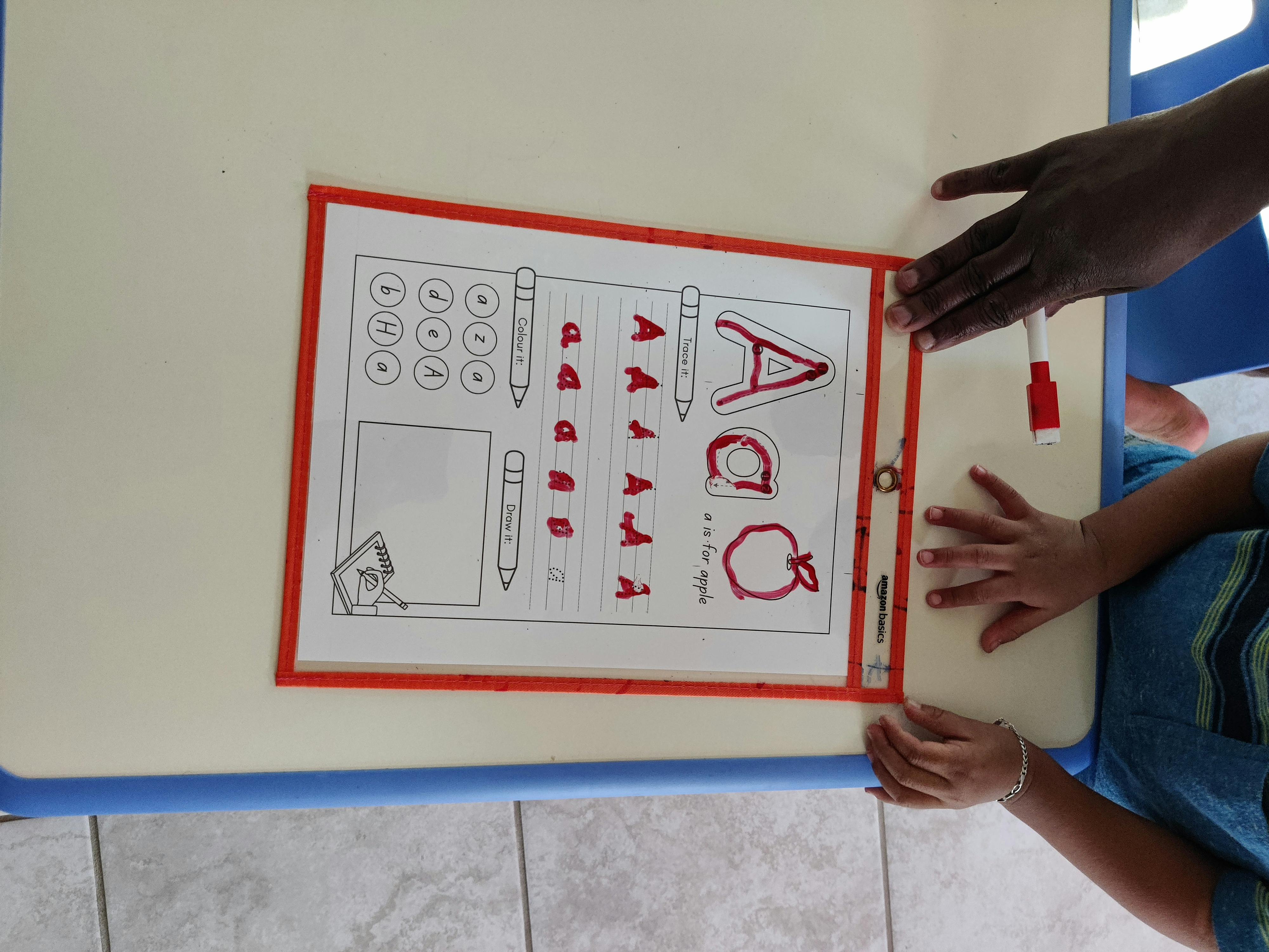 Two people's hands on a table with an alphabet learning sheet