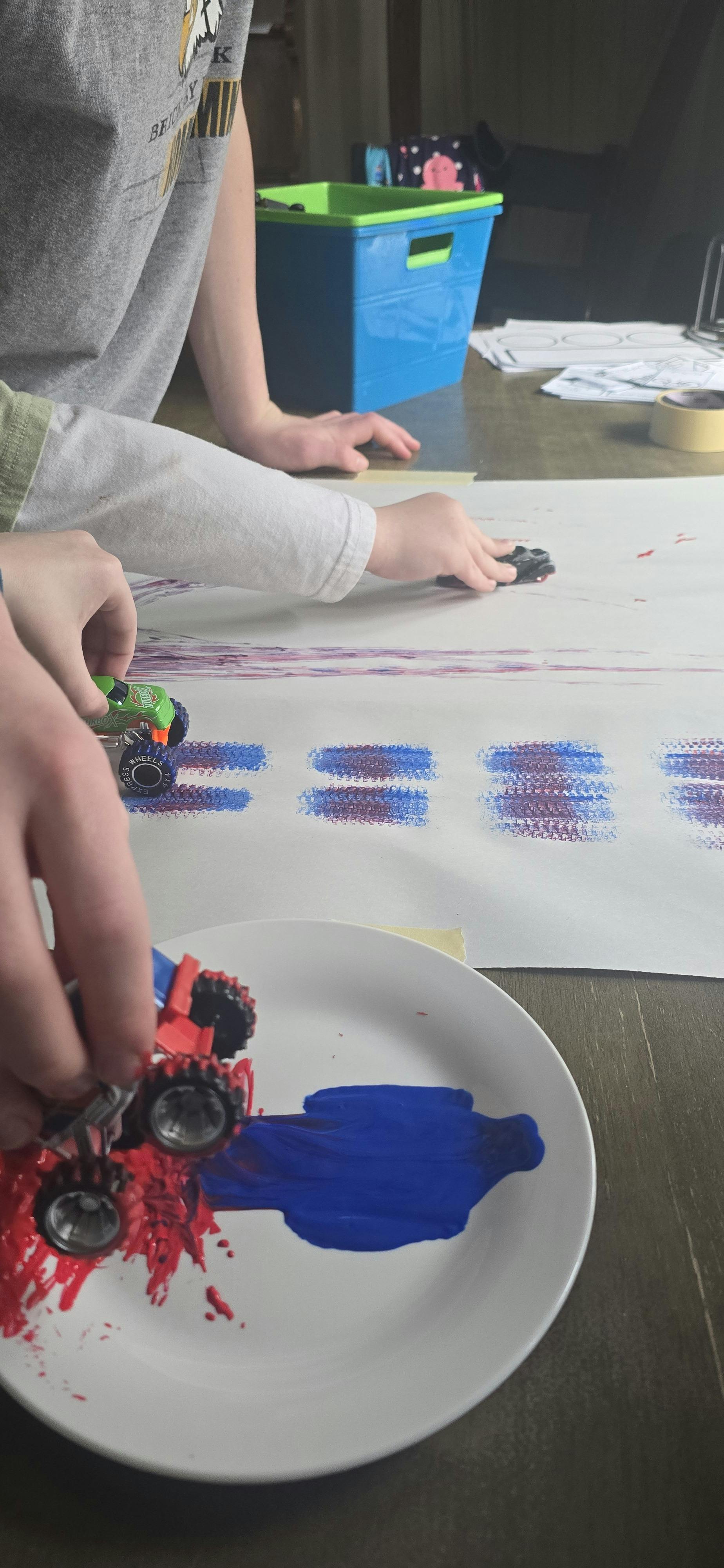 People rolling toy cars in paint and on paper