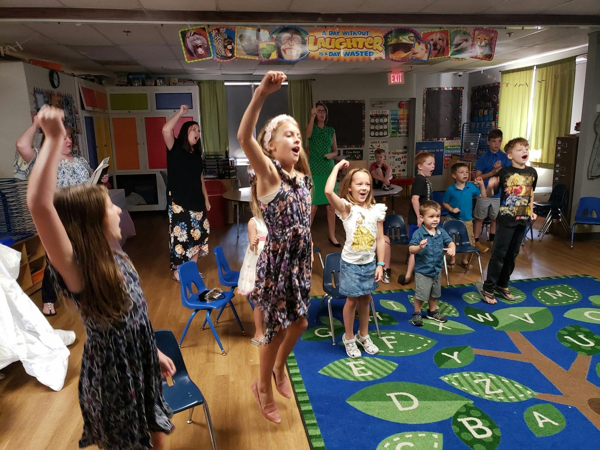 Children and adults raising their arms in a classroom