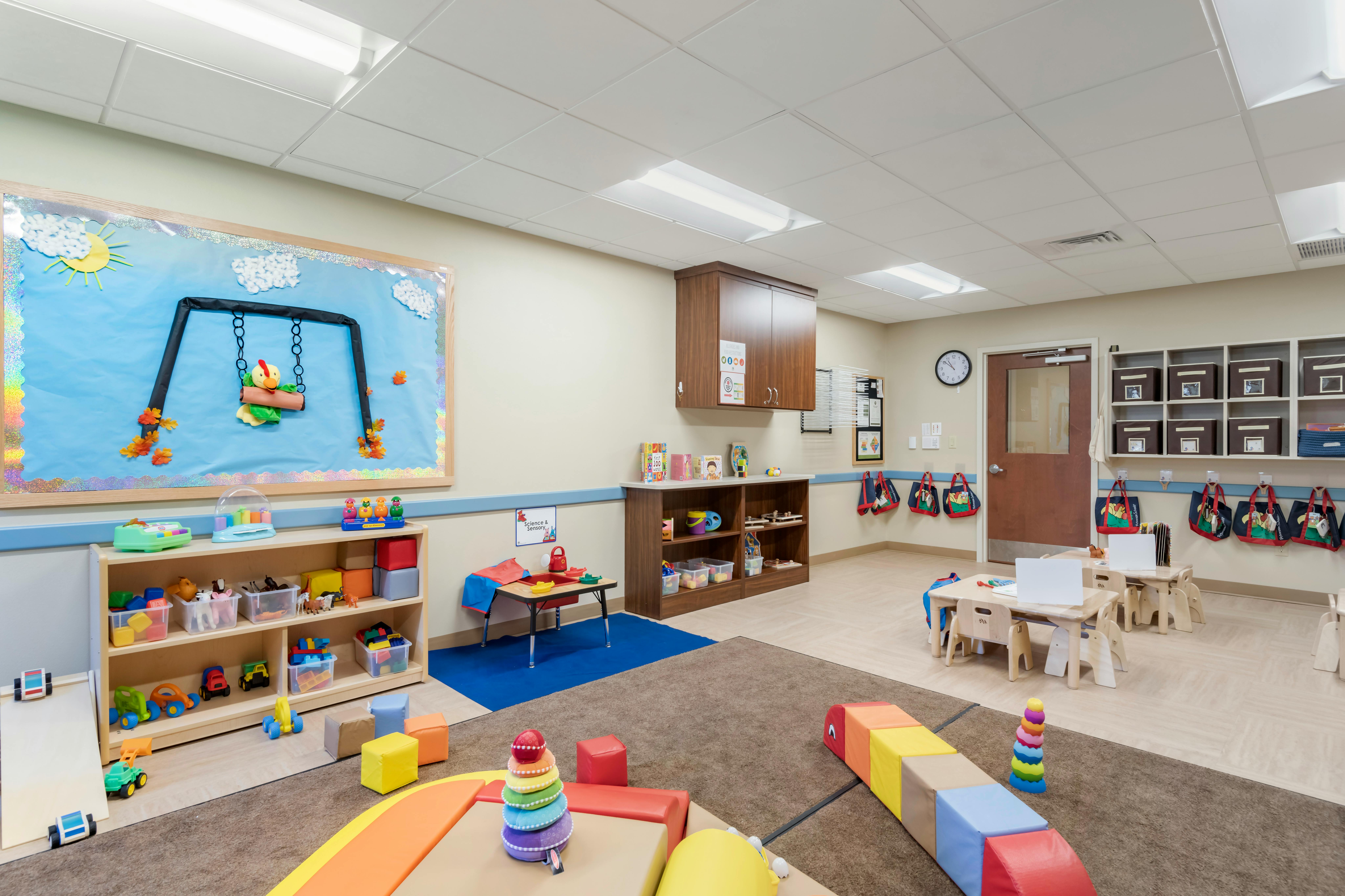 Classroom with child-sized tables, shelves of toys, and a colorful bulletin board