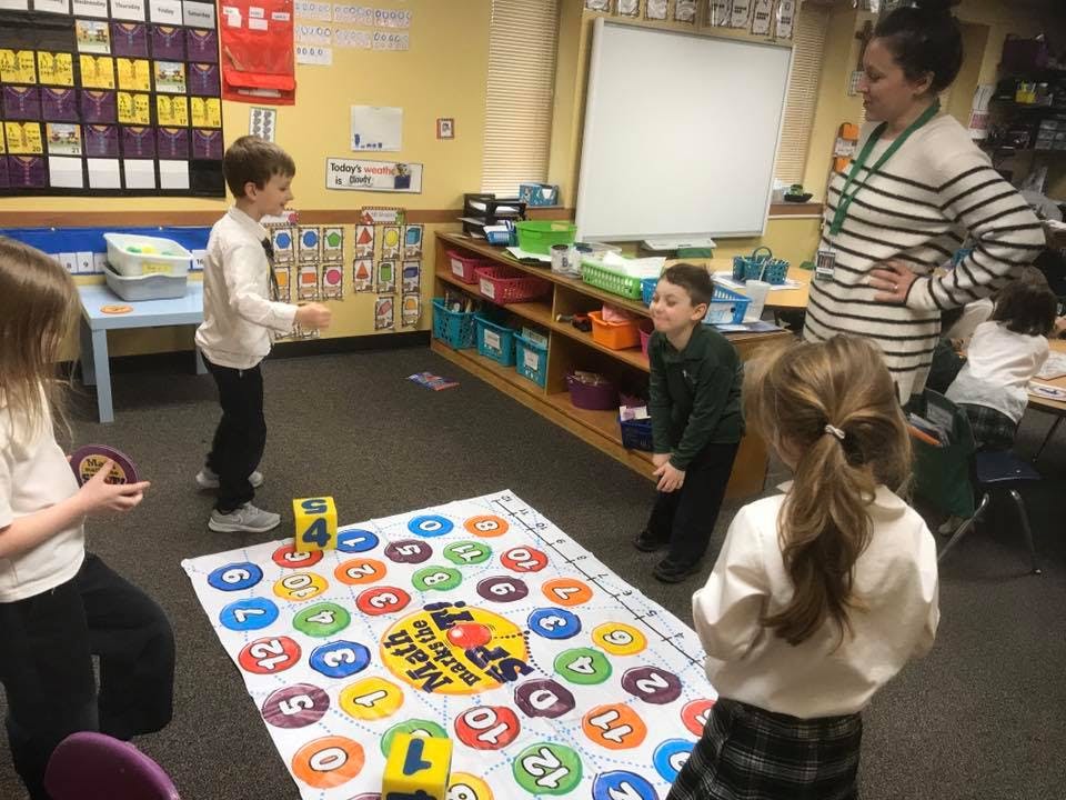 Children playing a board game on the floor with an adult supervising
