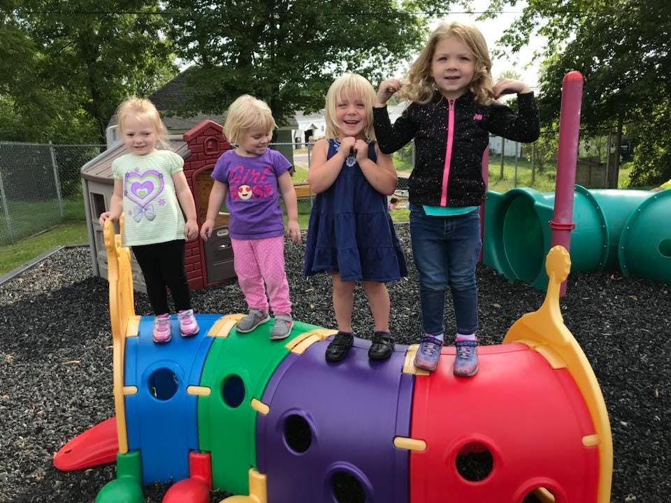 Four children standing on a colorful playground tunnel climber