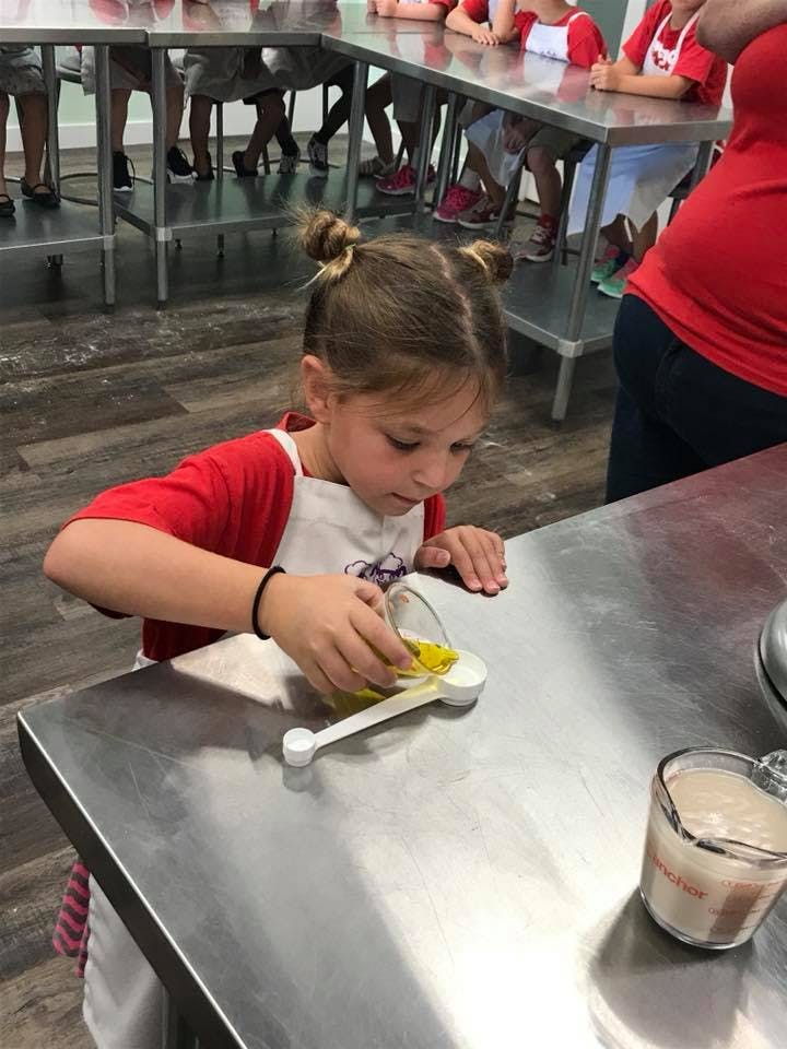 Child pouring liquid from a measuring cup into a spoon