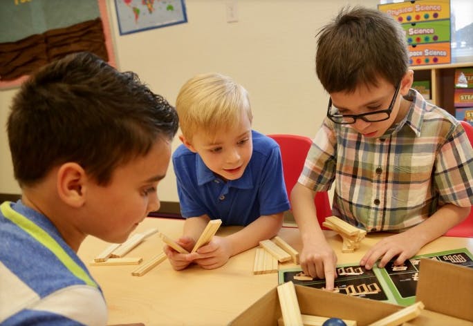 Three children playing with wooden blocks at a table in a classroom