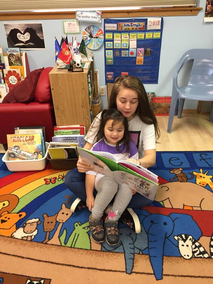 Teen and child sitting on a rug reading a book together