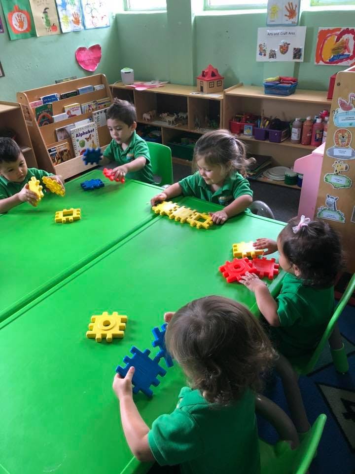 Children playing with interlocking gear toys at a green table
