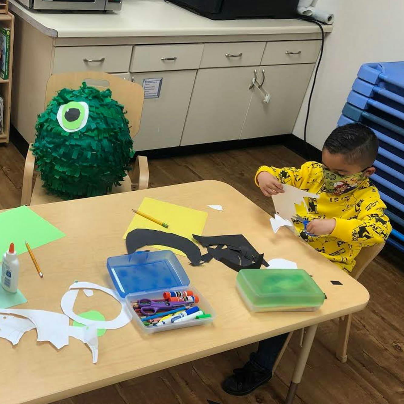Child cutting paper at a table with craft supplies