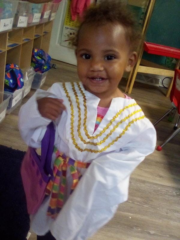 Child in white tunic with gold trim and colorful sash