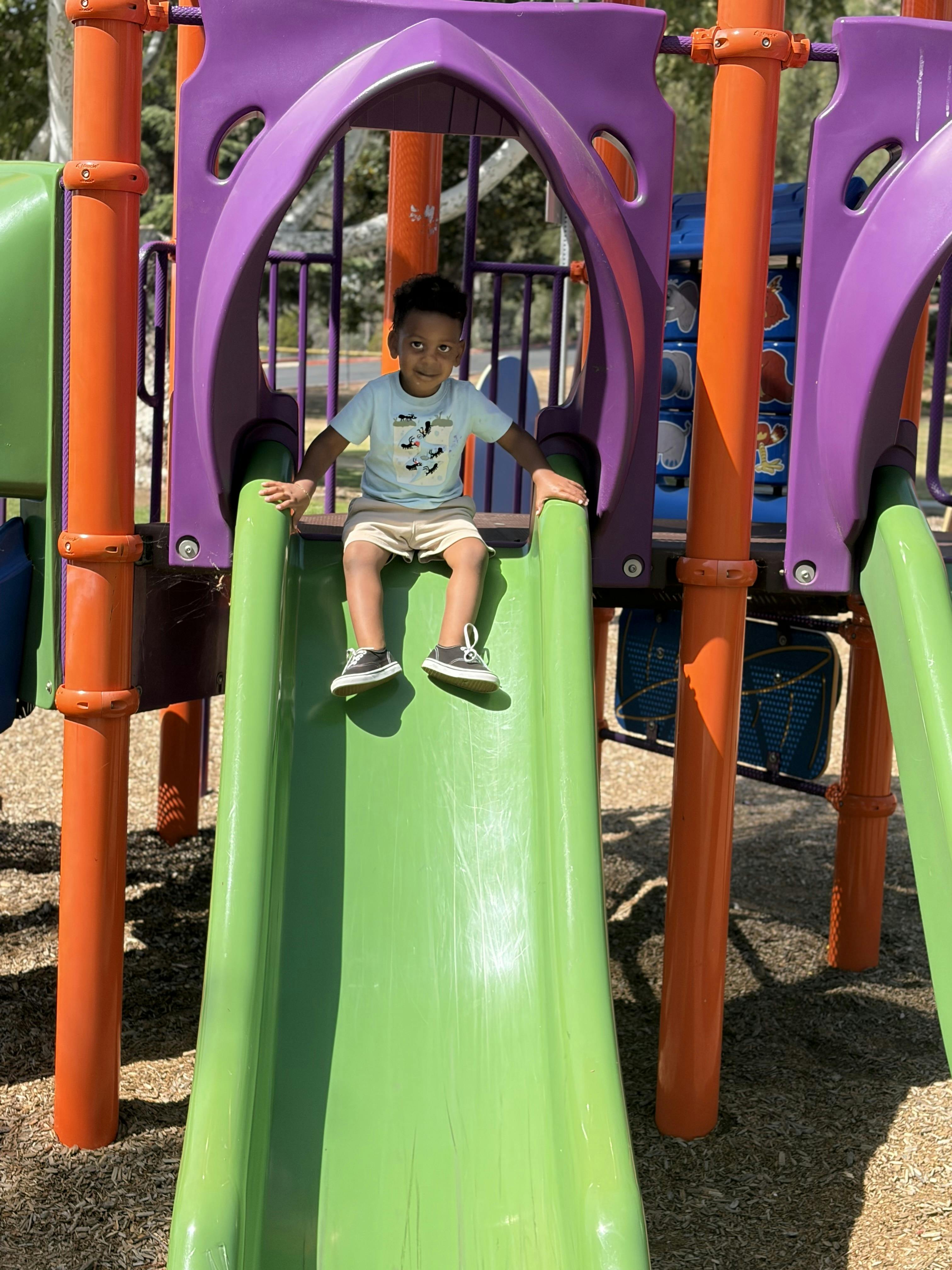 Child sitting at the top of a green playground slide