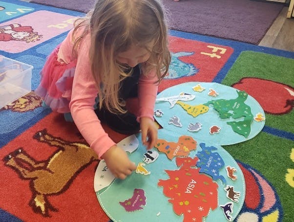 Child playing with a world map puzzle on the floor