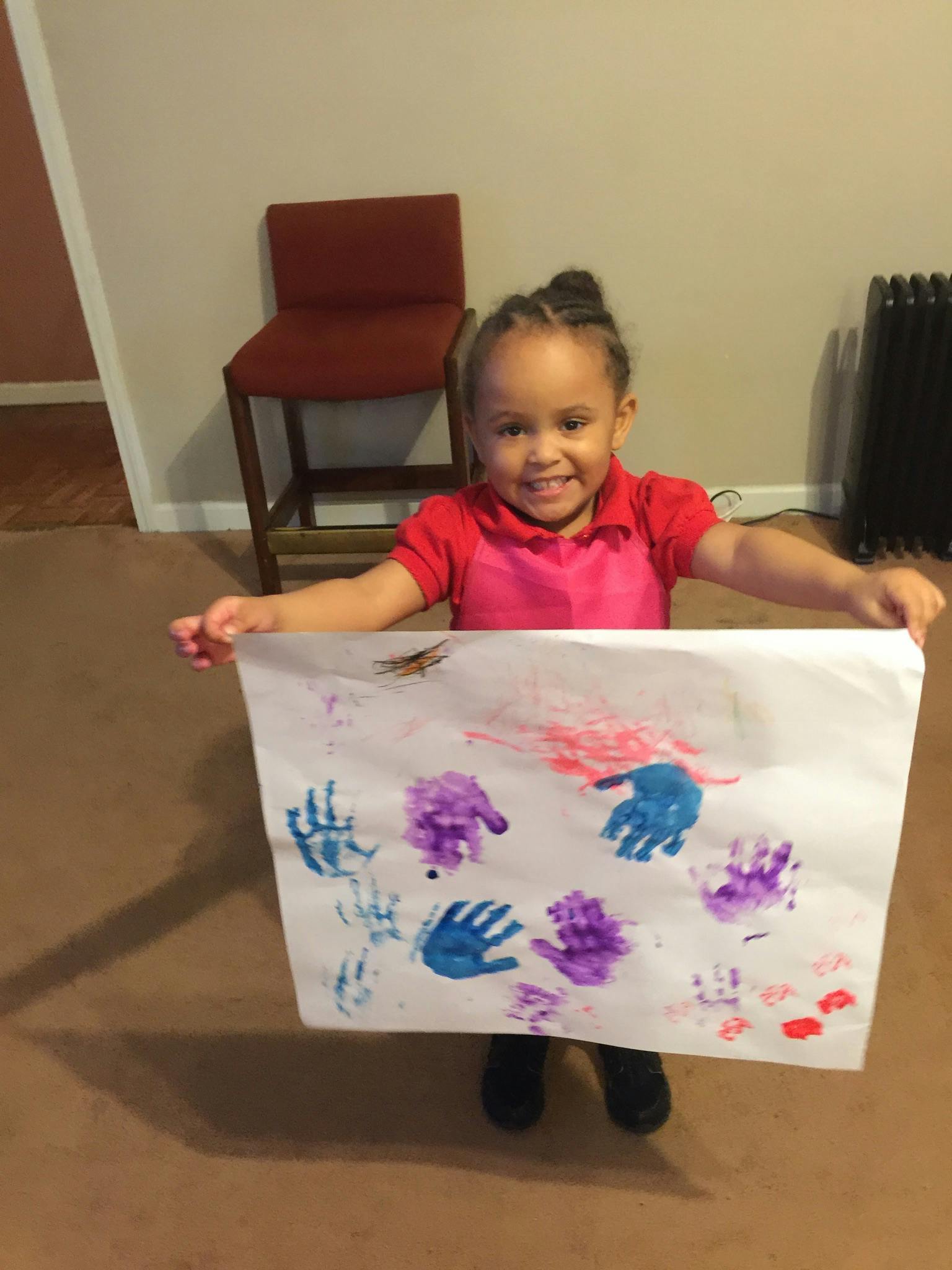 Child holding up a paper with colorful handprints