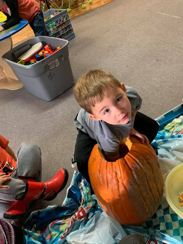 Child looking up while carving a pumpkin