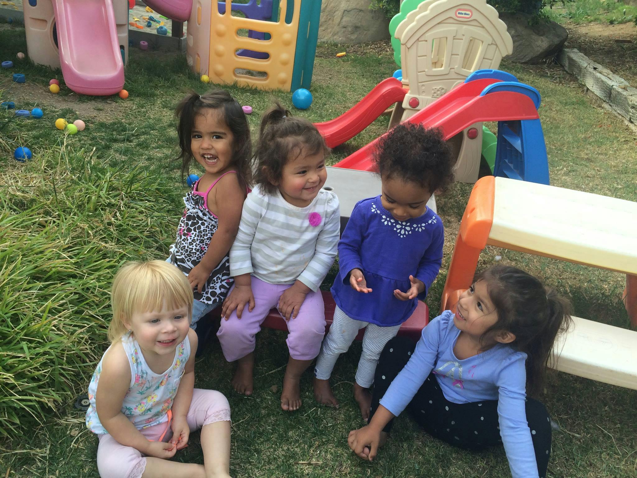 Five children sitting on grass near playground equipment