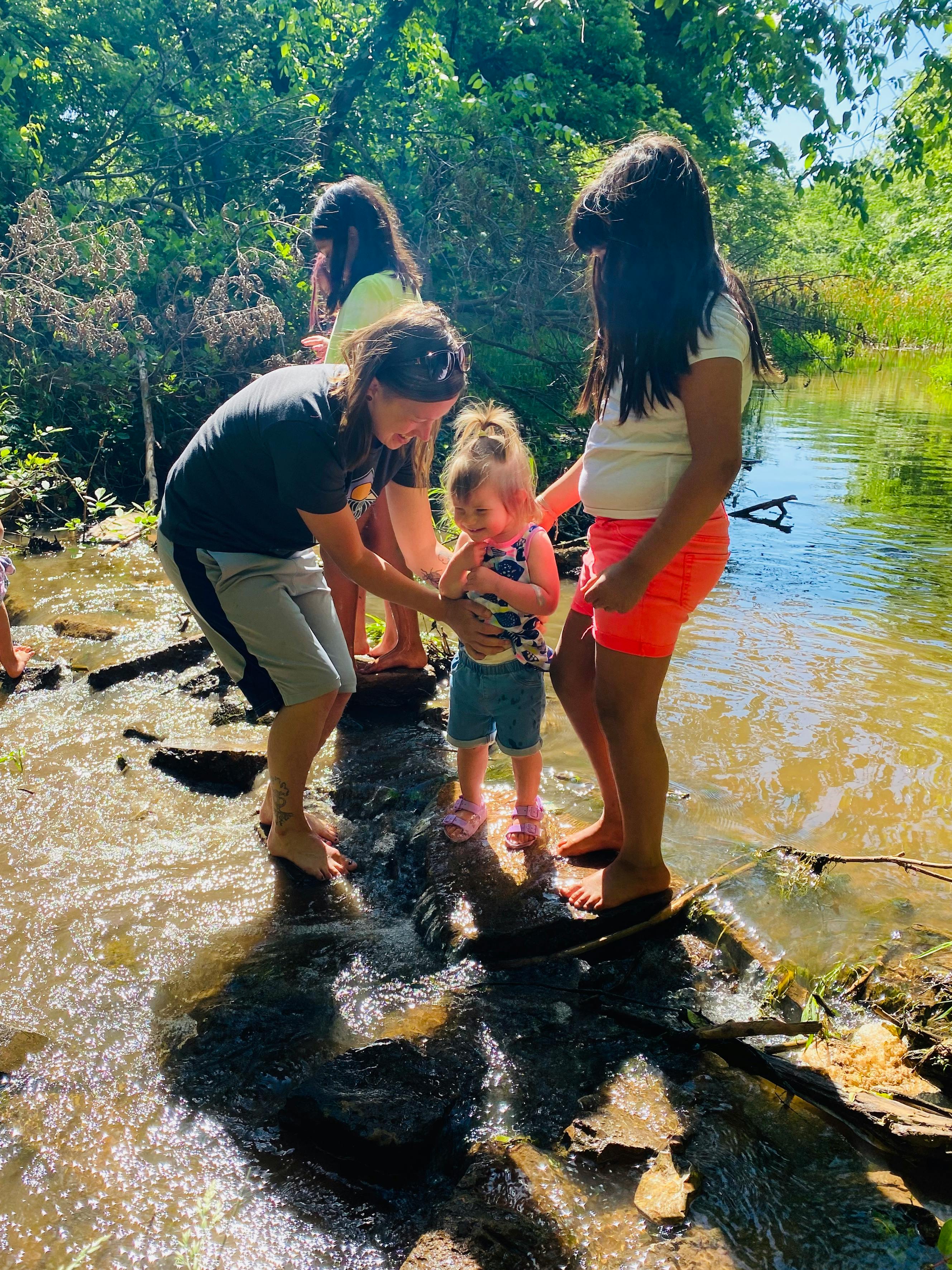 People helping a child cross a shallow stream