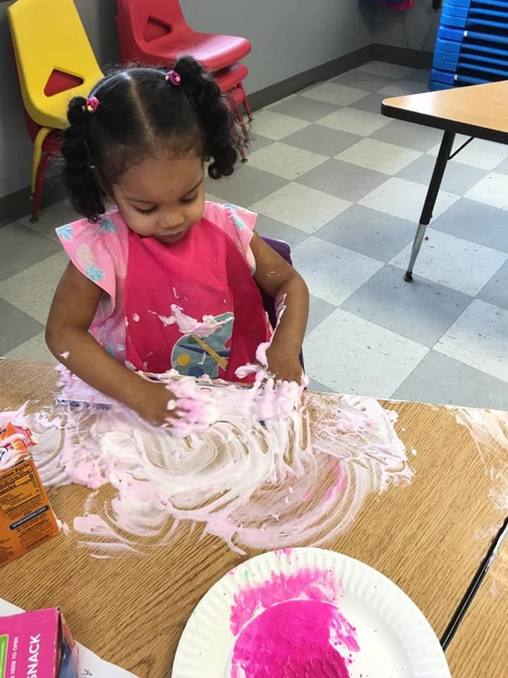 Child playing with pink shaving cream on a table