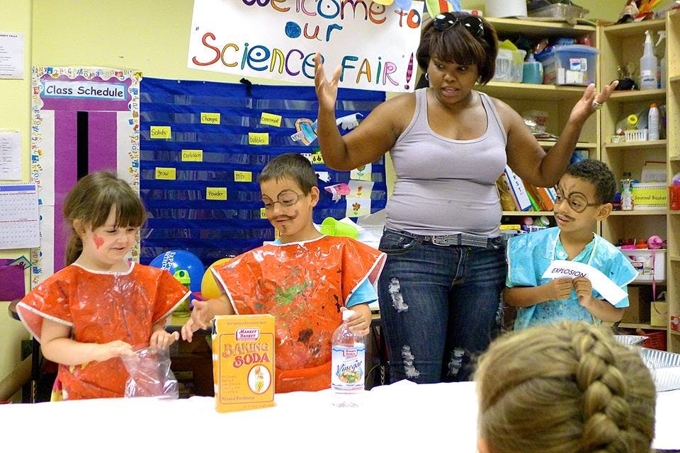 Adult and three children at a table with a "Science Fair" sign in the background