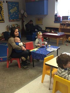 Adult holding an infant, child at a table in a classroom
